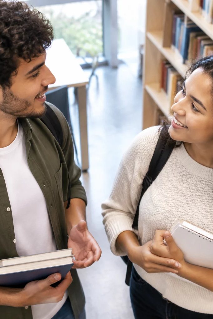 Duas participantes de pé conversando no corredor entre prateleiras de livros